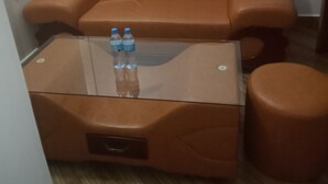 A brown leather sofa with a glass coffee table in front. Two water bottles are on the table.