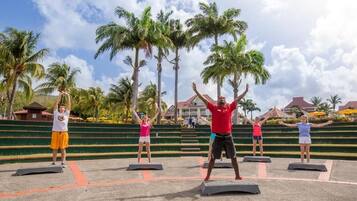 A group of people exercising on outdoor platforms with palm trees and a building in the background.