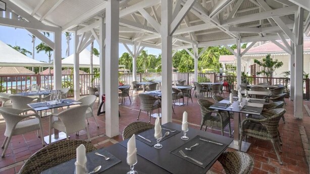 An outdoor patio area with tables and chairs, a pool in the background, and a white gazebo structure. - Studio Avec Piscine et Plages Accessibles à Pieds (Sainte-Luce)