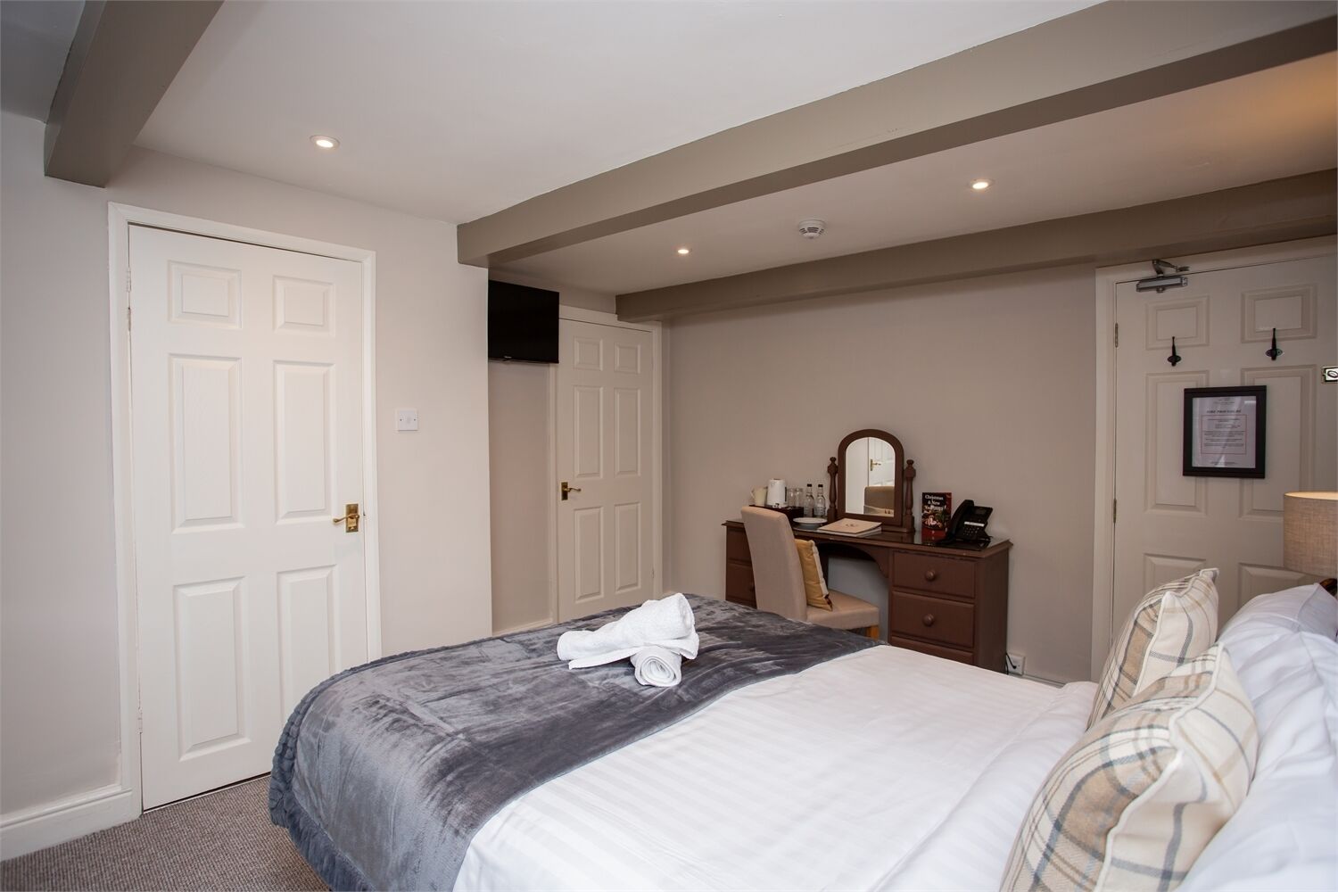 A hotel room with a bed, a desk with a chair, a mirror, and a door.