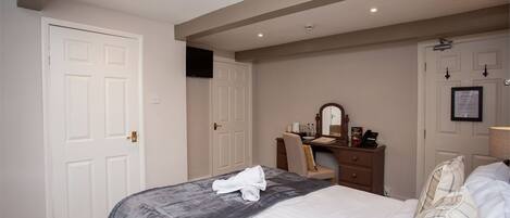 A hotel room with a bed, a desk with a chair, a mirror, and a door.