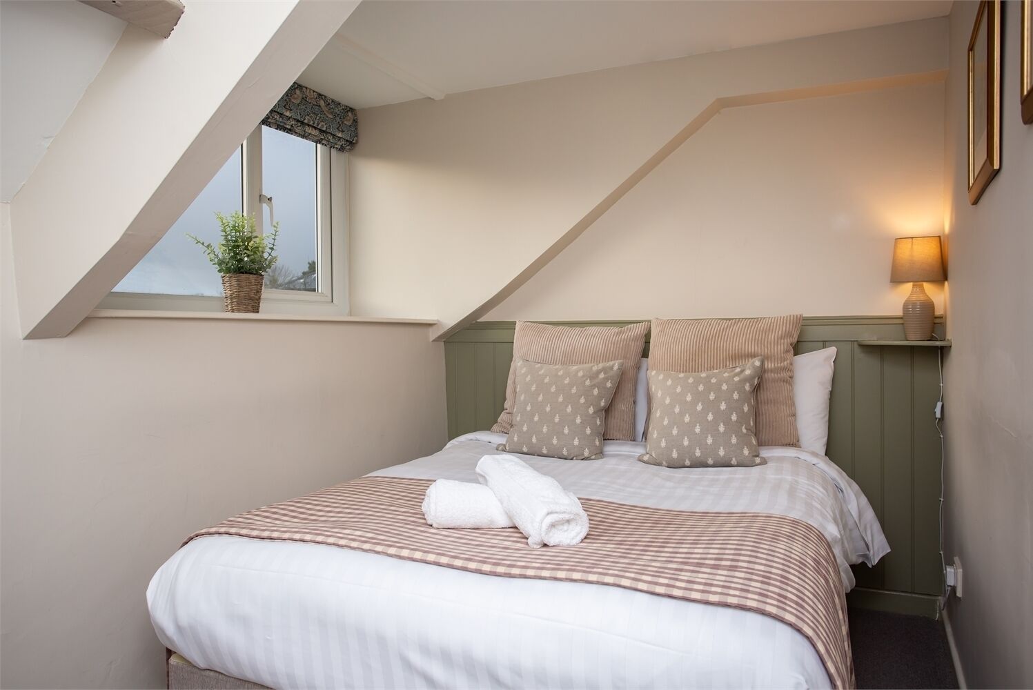 A bedroom with a sloped ceiling, a bed with striped bedding, and a bedside lamp.