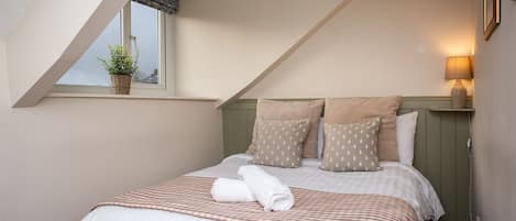 A bedroom with a sloped ceiling, a bed with striped bedding, and a bedside lamp.