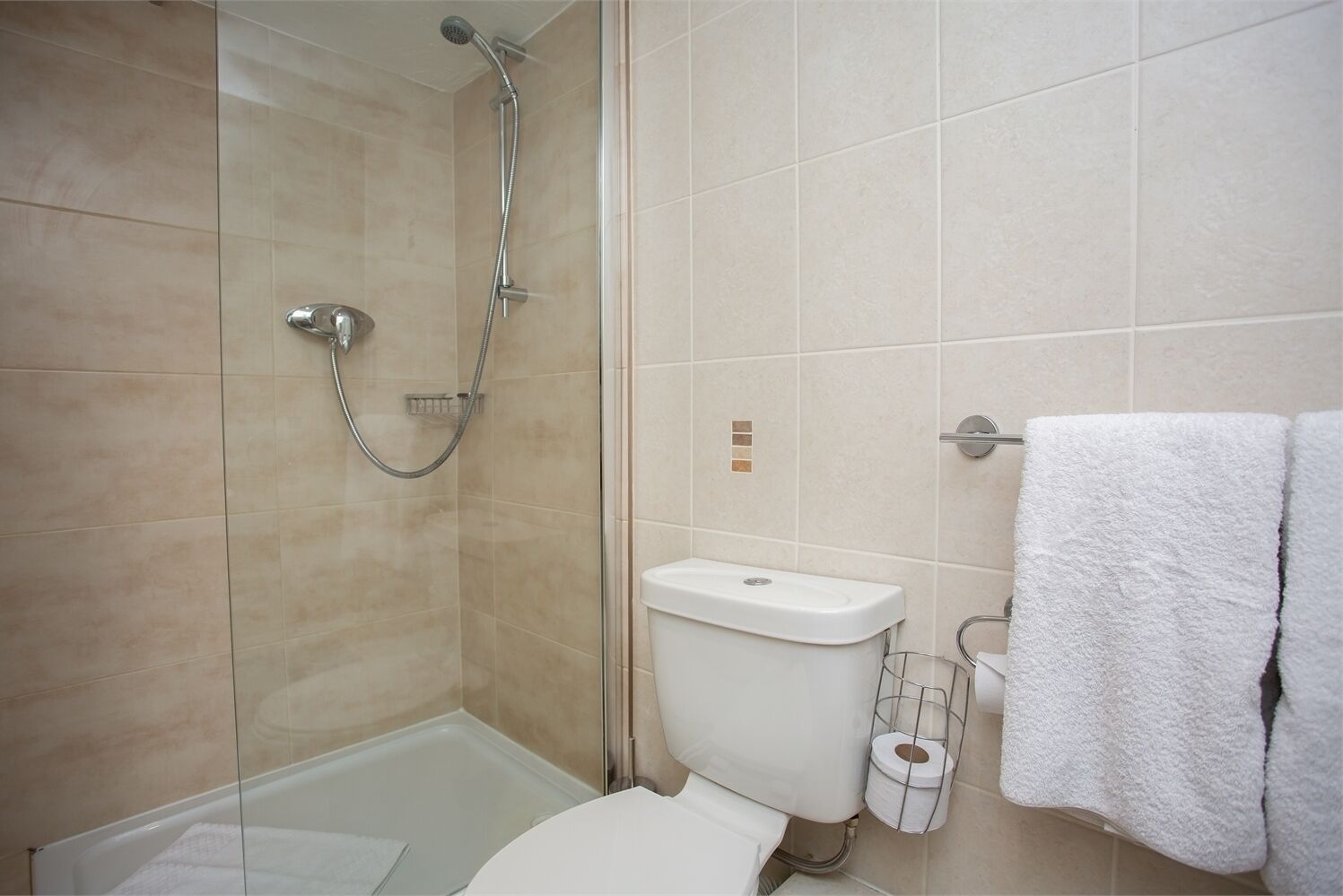 Une salle de bain avec une douche à parois de verre, des toilettes blanches et un porte-serviettes avec des serviettes blanches.