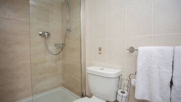 A bathroom with a glass-enclosed shower, a white toilet, and a towel rack with white towels.