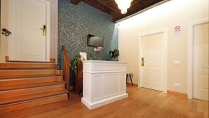 A room with wooden flooring, a white reception desk, a staircase, and a wall-mounted TV. - Golden Pantheon Rooms (Rome)