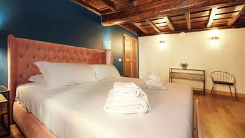A neatly made bed with white linens and a folded towel on top, a wooden headboard, and a wooden floor.