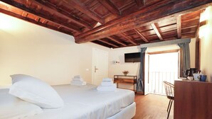A bedroom with a wooden ceiling, a bed with white linens, a desk with a chair, and a television on the wall. - Golden Pantheon Rooms (Rome)