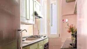 Une cuisine de taille réduite, équipée d’une cuisinière à gaz, d’un évier et de meubles de rangement verts.
