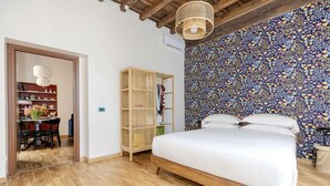 Une chambre avec un lit en bois, une armoire en bois, un coin repas avec une table et des chaises, et un mur orné d’un motif.