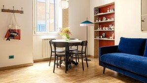 Une pièce comprenant une table à manger, des chaises, un canapé bleu, une bibliothèque et une fenêtre avec des volets.