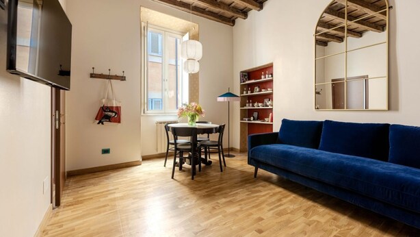 Un salon avec un plancher en bois, un canapé bleu, une table à manger avec des chaises, un luminaire suspendu et une bibliothèque.