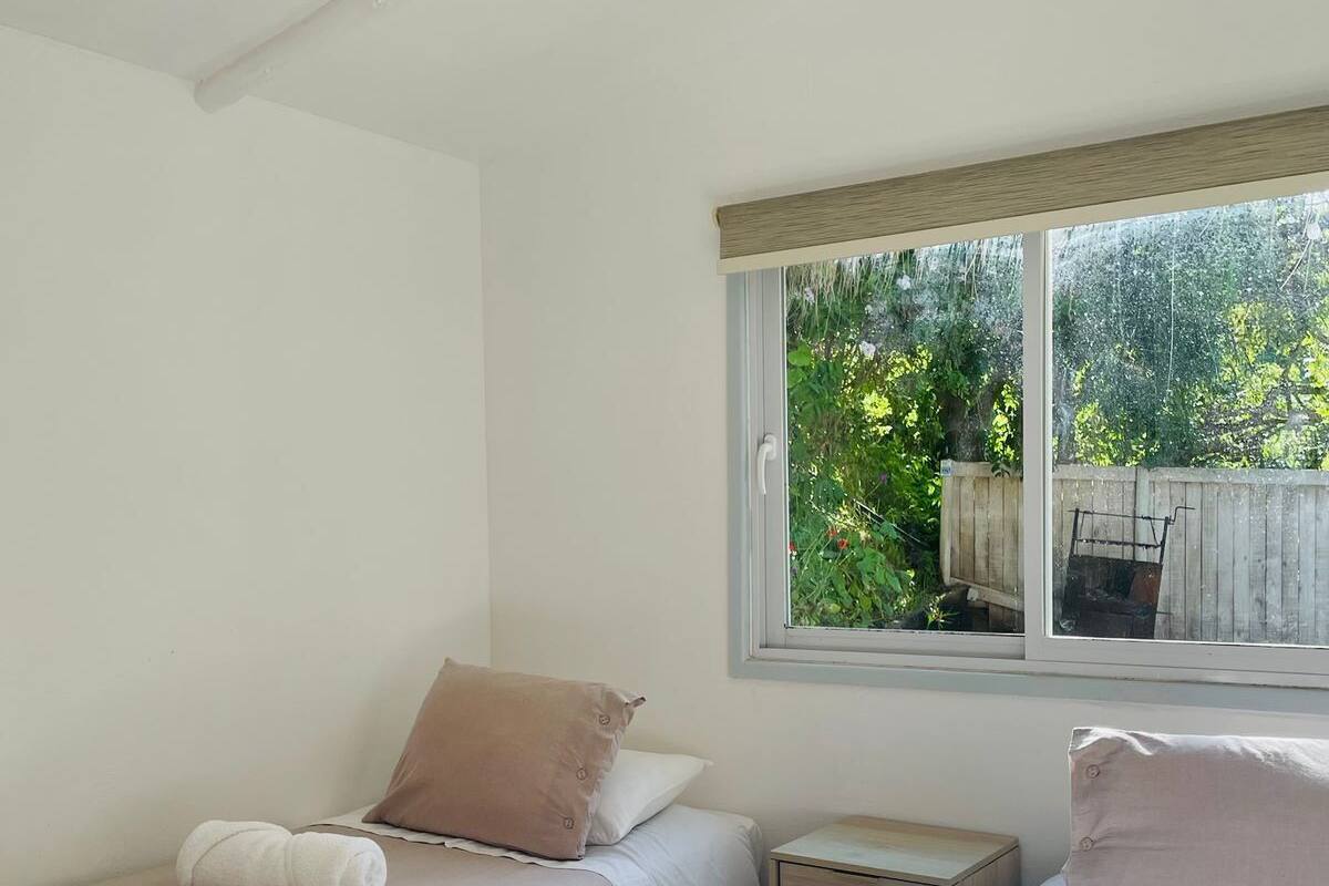 Un dormitorio con dos camas, una ventana con vistas a la vegetación y una mesita de noche pequeña.