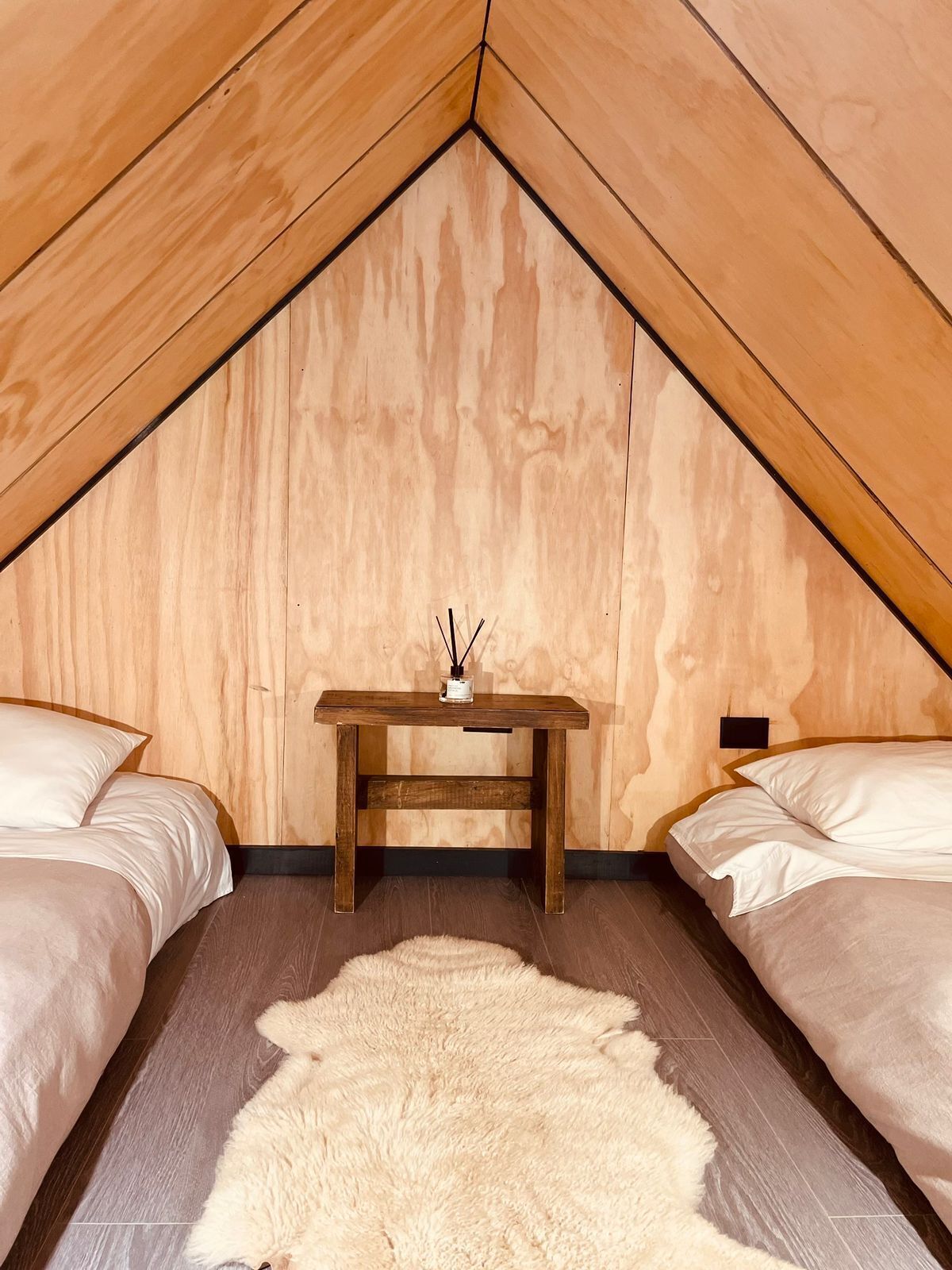 A cozy attic bedroom with two beds, a wooden table, and a fluffy rug.