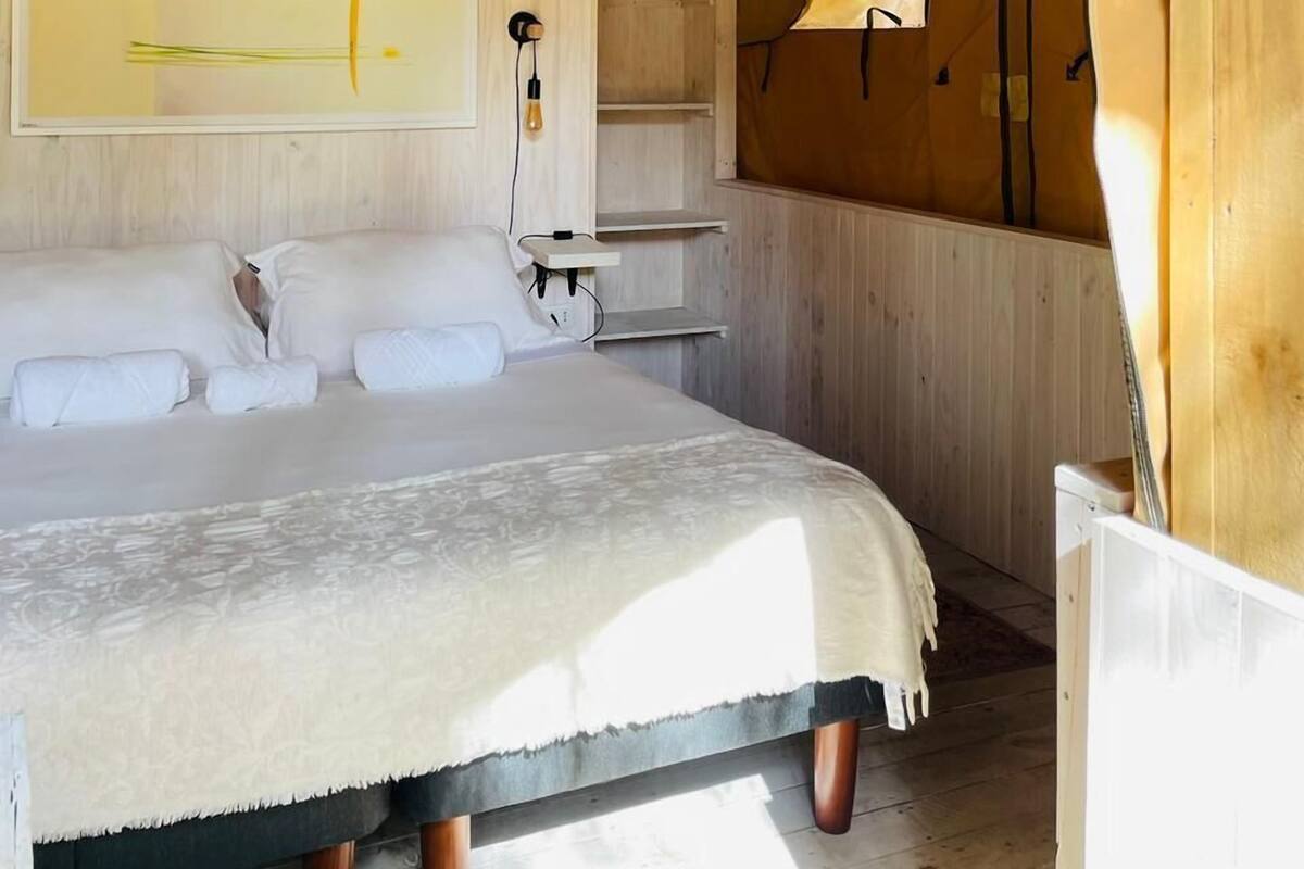 Una habitación con tienda de campaña, una cama, una lámpara colgante y una pared de madera.