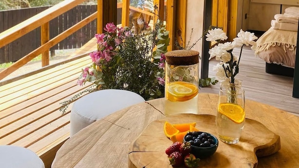 A wooden deck with a table set for a meal, surrounded by a wooden railing and a view of greenery. - Parque Laguna de Zapallar (Zapallar)