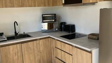 Cozinha moderna com armários de madeira, micro-ondas embutido, máquina de café e frigorífico de aço inoxidável.