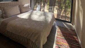 A bedroom with a large window, wooden ceiling, and a bed with a patterned bedspread. - Parque Laguna de Zapallar (Zapallar)