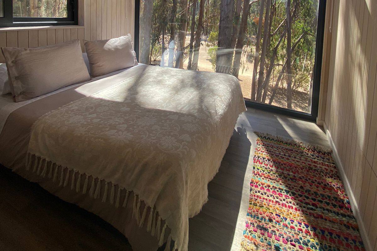 Un dormitorio con un ventanal grande, techo de madera y cama con colcha estampada.
