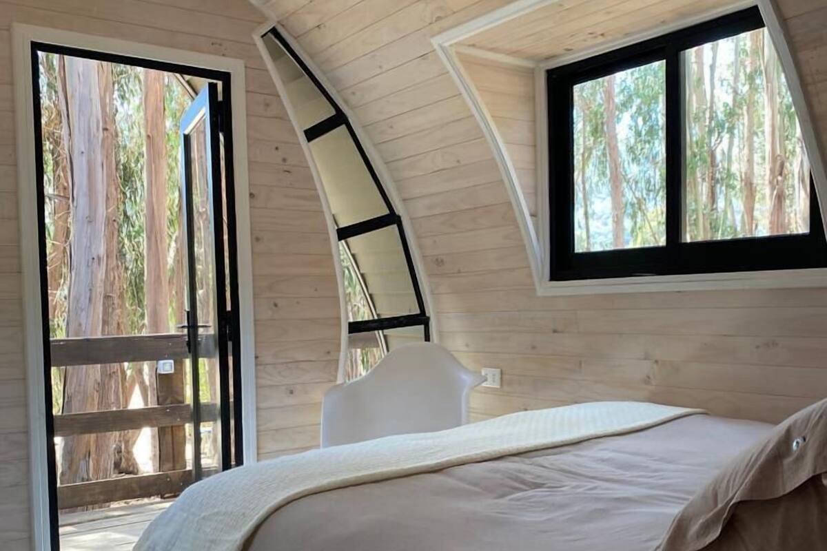 Un dormitorio con una cama grande, una ventana y vista a árboles.