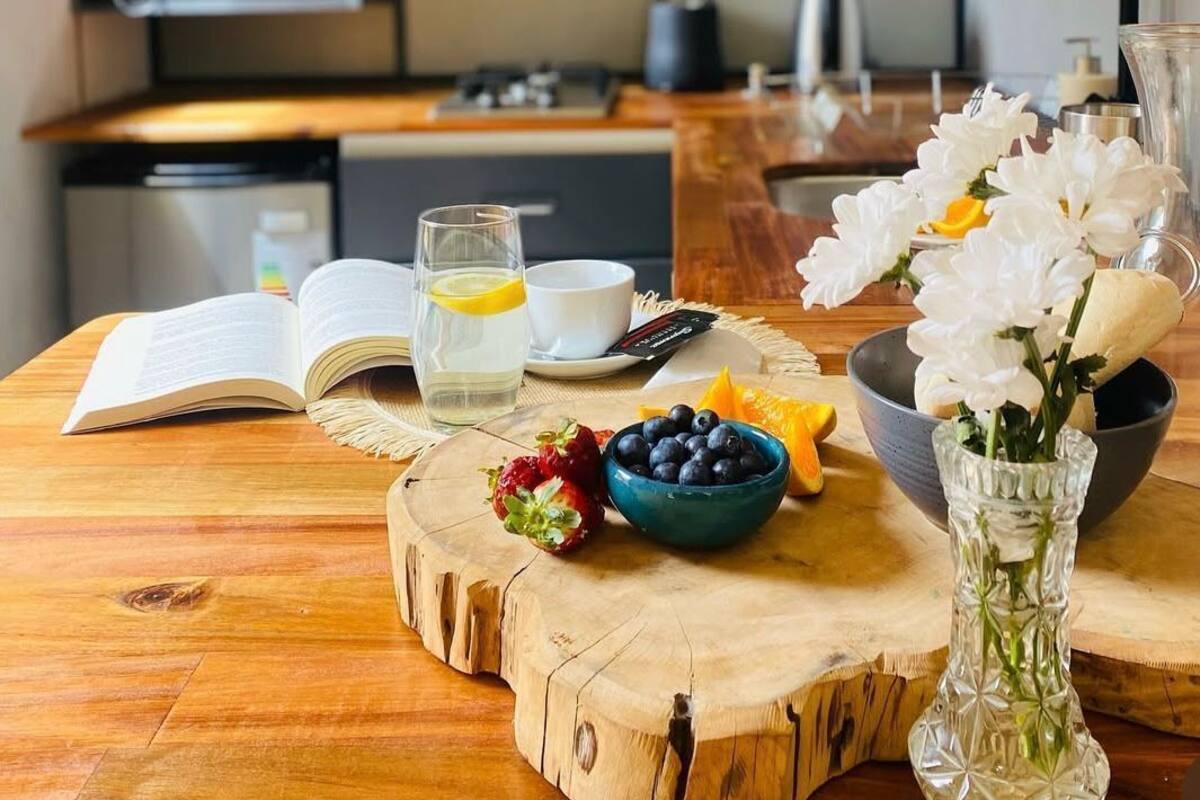 Una cocina moderna con electrodomésticos integrados, una mesa de comedor de madera con un libro, un vaso de agua y fruta fresca.