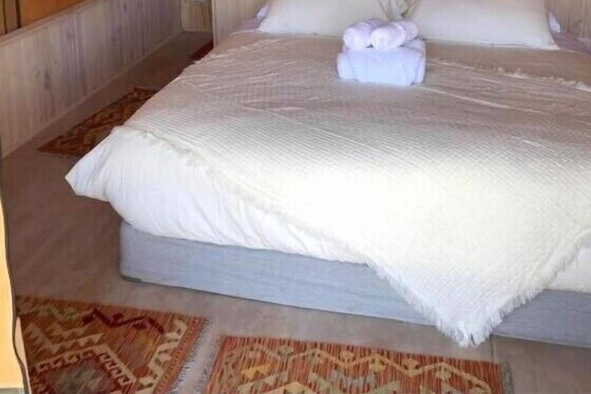 Habitación individual con una cama de madera, un cabecero de madera, una ventana pequeña y un tapete estampado en el suelo.
