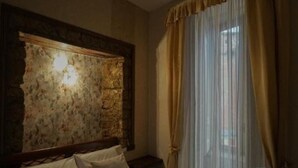 A hotel room with a bed, a nightstand, a stone accent wall, and sheer curtains. - Posillipo Apartment (Napoli)
