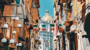 A narrow street with buildings on either side, a clear blue sky, and a domed structure in the distance. - Posillipo Apartment (Napoli)