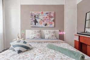 Un dormitorio con cama, almohadas, un letrero de neón, una obra de arte en la pared y un aparador.