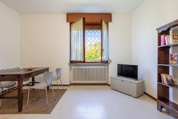 Un coin repas avec une table en bois, des chaises, un radiateur, un téléviseur et une bibliothèque.