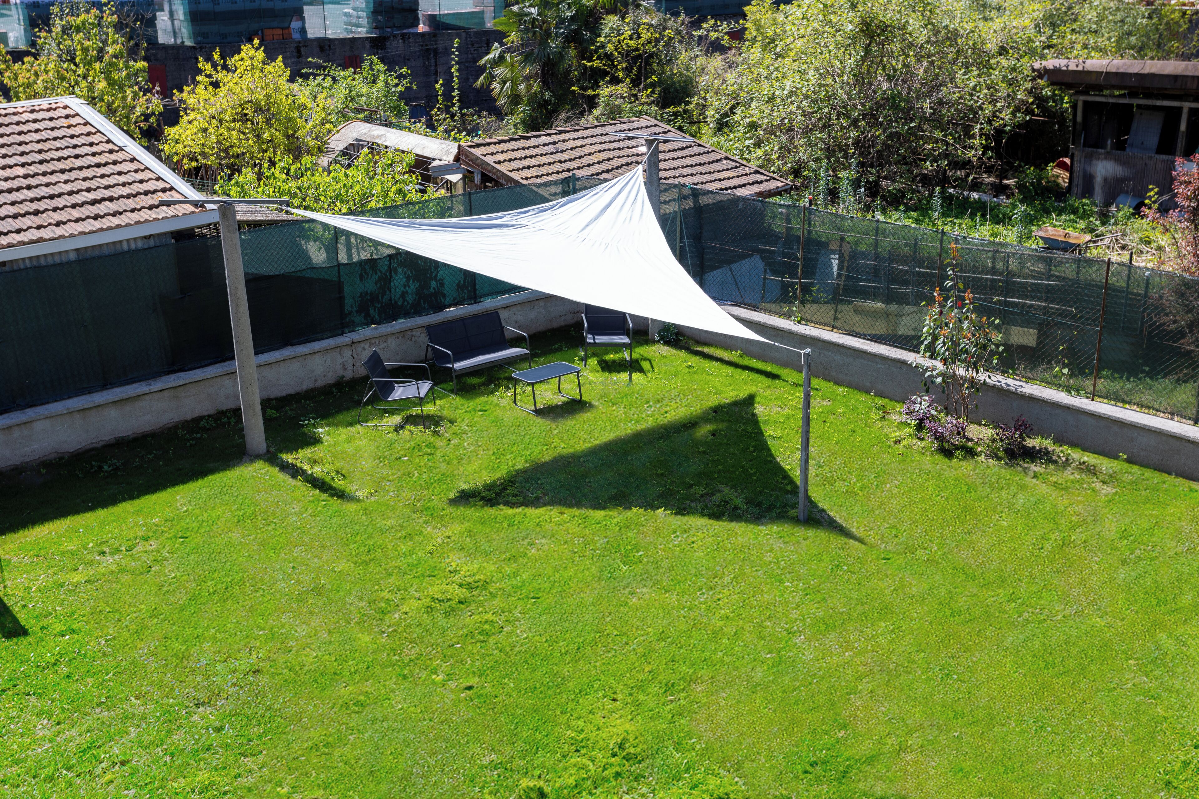 A residential area with a grassy yard, a white canopy, and a fenced garden.
