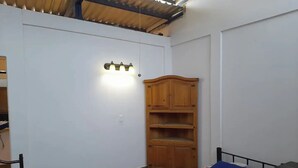 A small, simple room with a bed, a wooden cabinet, and a wall-mounted light fixture. - Central Location -"FRIDA" (Cabo San Lucas)