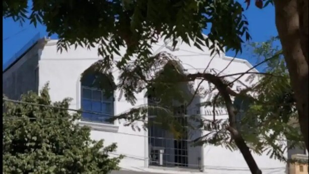 A white building with a large tree in front, a gated entrance, and a parked white car. - Central Location -"FRIDA" (Cabo San Lucas)