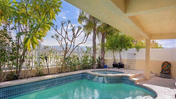Una piscina amb vora de rajola, envoltada de plantes i una tanca blanca.