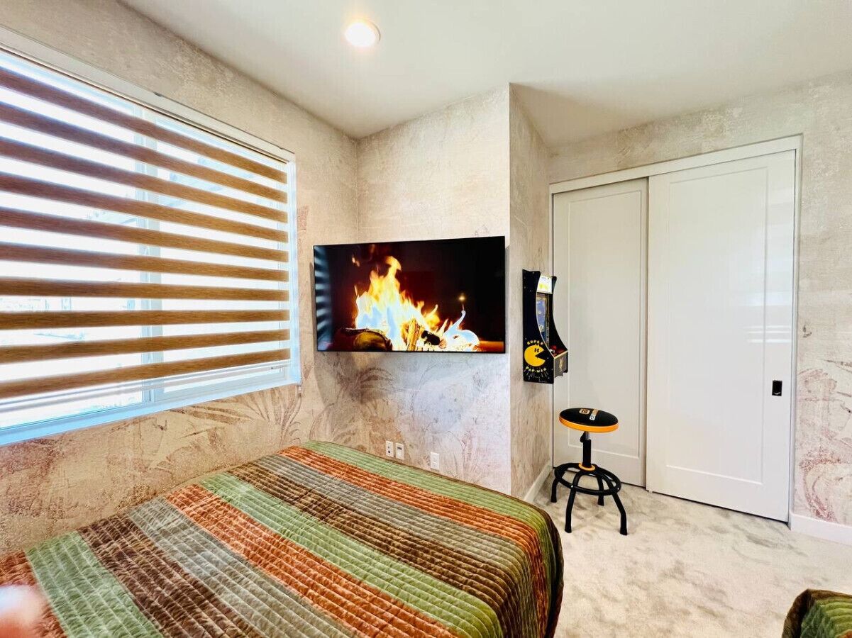 A bedroom with a bed, a television mounted on the wall, a door, and a window with blinds.