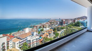 Une chambre d’hôtel située dans un immeuble de grande hauteur, offrant une vue panoramique sur l’océan et dotée d’un balcon avec une balustrade en verre.