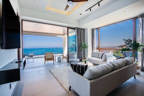 Una sala de estar moderna con un sofá grande, un televisor y vista al mar.
