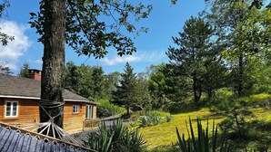 A wooden cabin with a sloped roof, surrounded by a lush garden and tall trees.