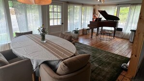 A dining area with a round table, chairs, a piano, and large windows.