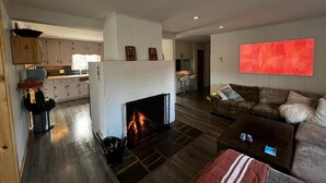 A spacious living area with a fireplace, a kitchen in the background, and a modern abstract painting on the wall.