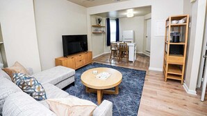Een moderne woonkamer met een bank, salontafel, televisie en een eethoek met stoelen en een tafel.