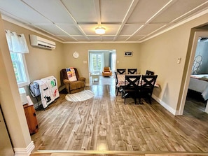 A living room with a fireplace, a dining area with a table and chairs, and a hallway leading to a bedroom.