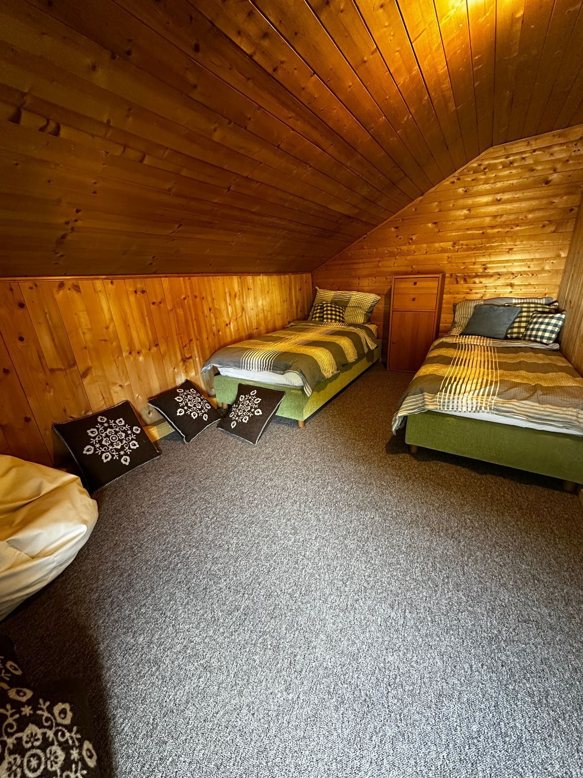 Ein gemütliches Schlafzimmer im Dachgeschoss mit Holzwänden, einem Etagenbett, zwei Nachttischen und einer grünen Polsterbank.