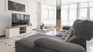 A modern living room with a flat-screen TV, grey sofa, and a large window with sheer curtains. - Charming flat for 6 people in Felanitx, Mallorca (Felanitx)
