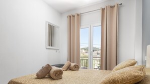 A bedroom with a bed, a window with curtains, a view of buildings, and a small table with towels. - Charming flat for 6 people in Felanitx, Mallorca (Felanitx)