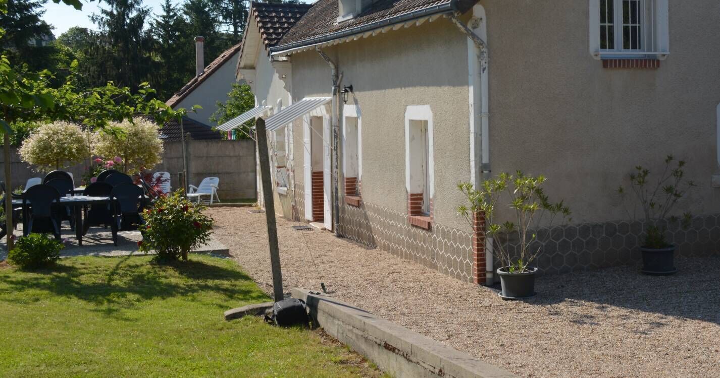 A house with a gravel driveway, a small garden with potted plants, and outdoor furniture.