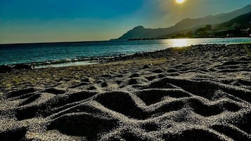 A beach with a clear sky and the sun setting or rising over the water.