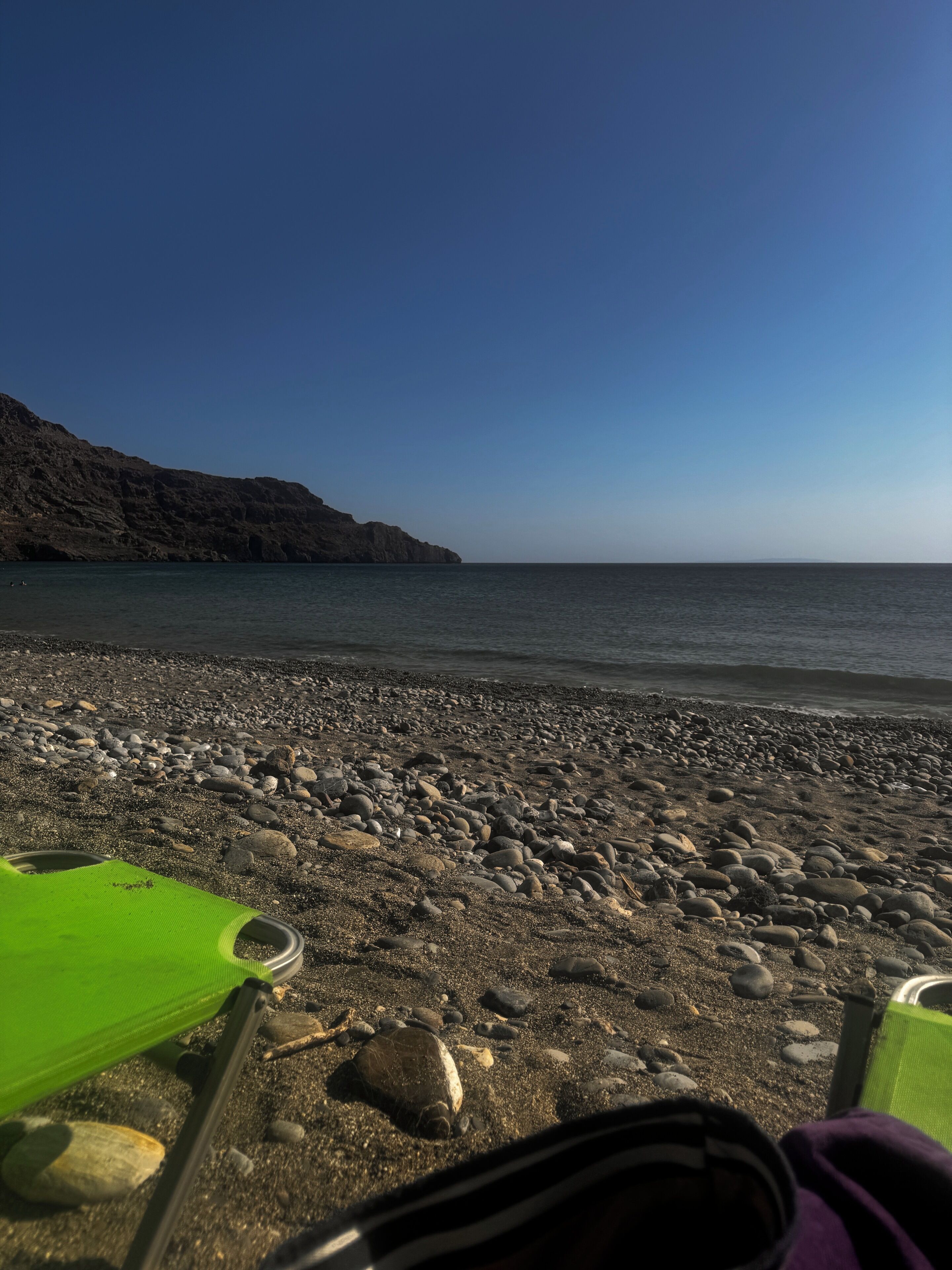 A rocky beach with a clear view of the sea and a distant mountain.