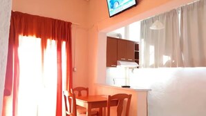 Ein Zimmer mit Esstisch und Stühlen, einem an der Wand befestigten Fernseher und einem Fenster mit Vorhängen.
