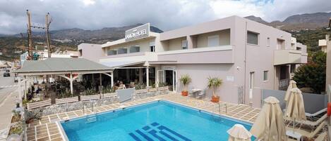 A hotel with a swimming pool, outdoor seating, and a view of mountains.